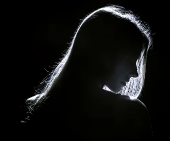 A woman's silhouette in shadow against a dark background, with her hair and outline illuminated.