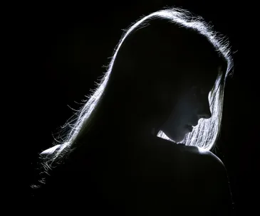 A woman's silhouette in shadow against a dark background, with her hair and outline illuminated.