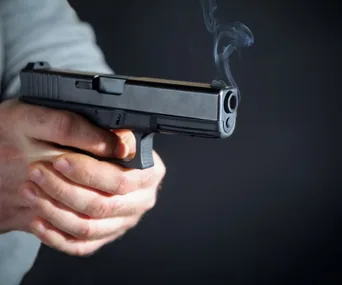 A person holding a smoking handgun against a dark background.