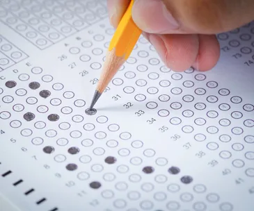 A hand marks answers on a multiple-choice test sheet with a pencil, focusing on questions in the 30s.