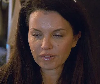 A woman with long dark hair appears emotional, having teary eyes and a slight frown.