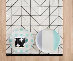 Plates and a mug with geometric designs on a patterned table runner.