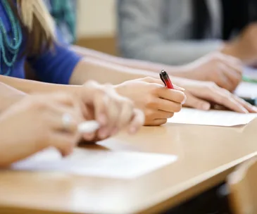 Students writing on paper during an exam, focusing on hands with pens.