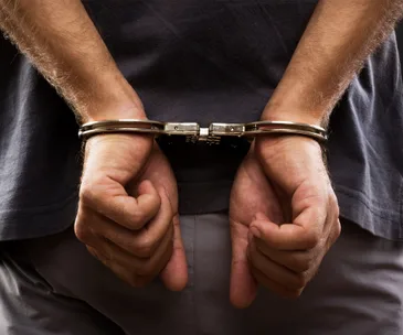 Individual in handcuffs wearing a dark shirt and visible back view.