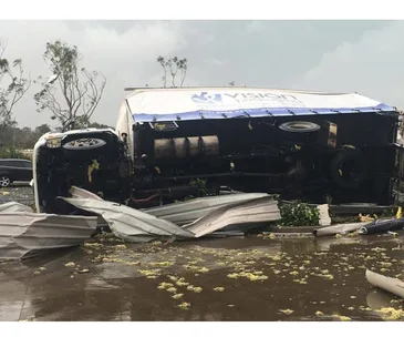 Overturned truck with Vision Logistics logo amid debris on a rainy day.
