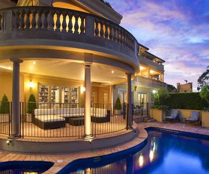 Luxurious mansion with a pool, elegant terrace, and ambient lighting under a vibrant evening sky.