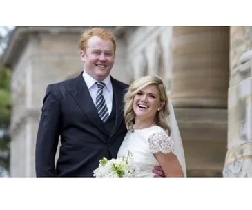 A bride and groom smiling joyfully outside a historic building, with the bride holding a bouquet of white flowers.