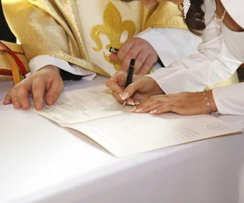 Bride signing a marriage document, overseen by a person in ceremonial attire.