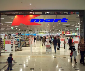 Entrance of a Kmart store with people walking in a shopping mall setting.