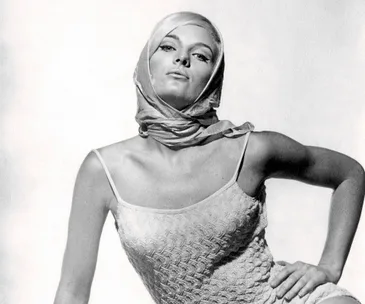 Young woman in a textured dress and headscarf, posing confidently against a plain background.