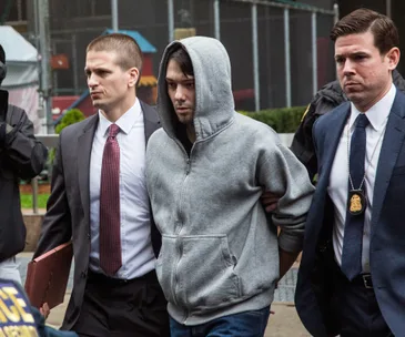 Man in a gray hoodie handcuffed and escorted by officers in suits outside.