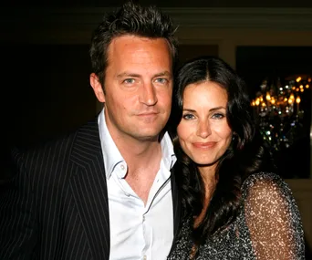 A man and a woman smiling and posing together at a formal event with chandeliers in the background.