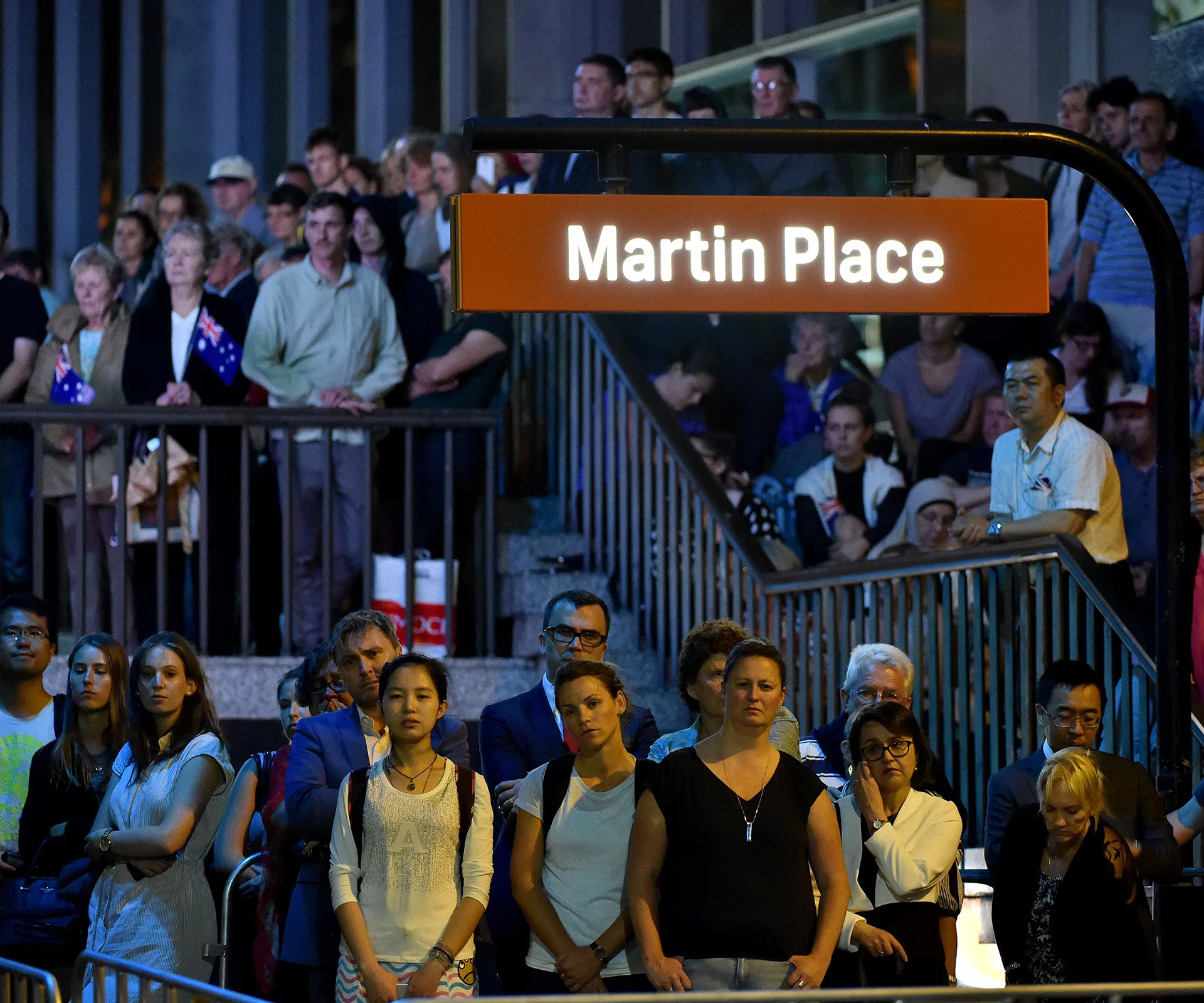 Crowd gathers at Martin Place, Sydney, watching a public event with calm expressions at night.