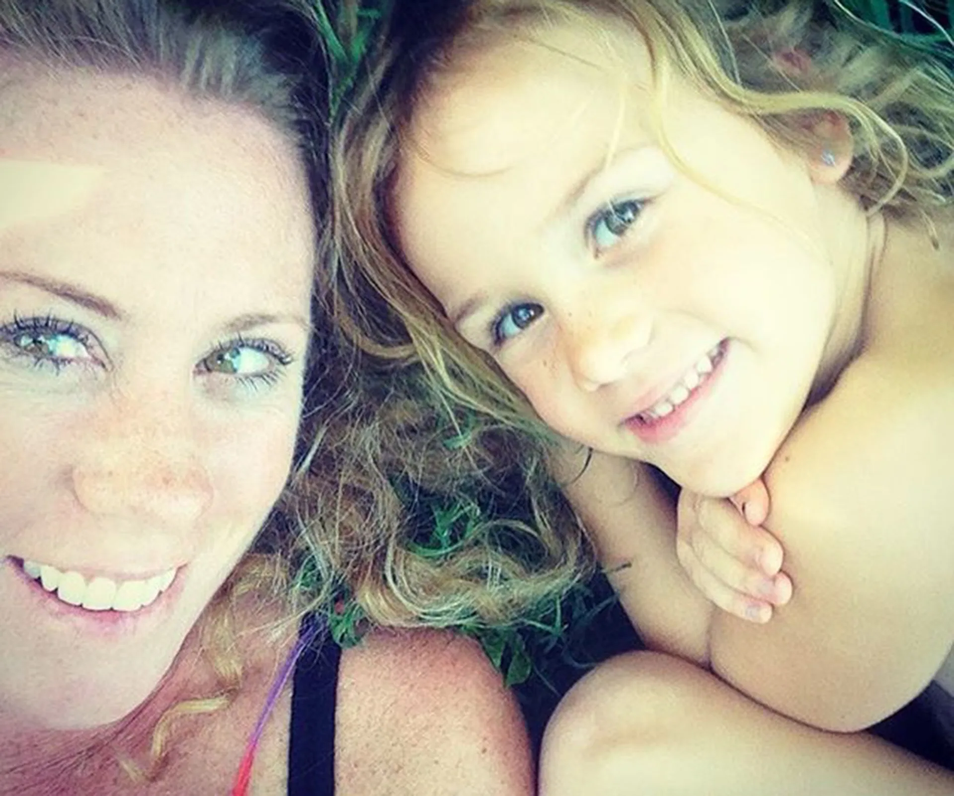 Mother and young daughter lying on grass, smiling.