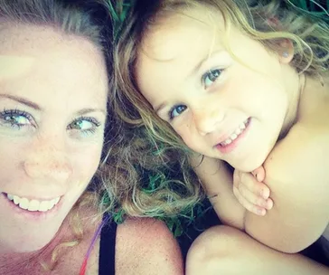 Mother and young daughter lying on grass, smiling.