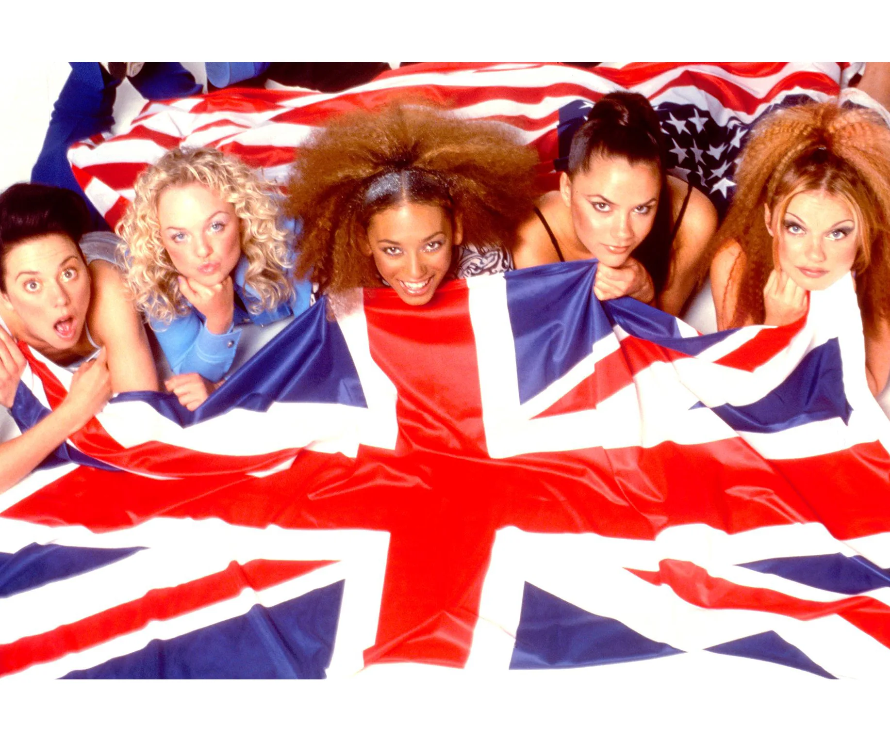 Five women lying down, partially covered by a large British flag, smiling at the camera.