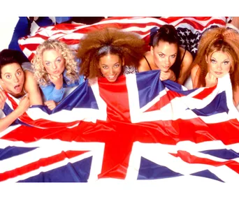 Five women lying down, partially covered by a large British flag, smiling at the camera.