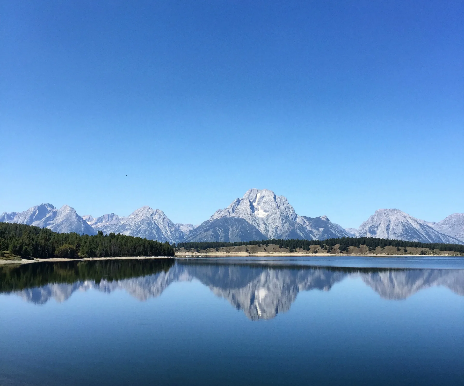 Serene mountain landscape with clear blue lake reflecting the jagged peaks and a bright sky at Yellowstone.