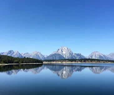 Serene mountain landscape with clear blue lake reflecting the jagged peaks and a bright sky at Yellowstone.