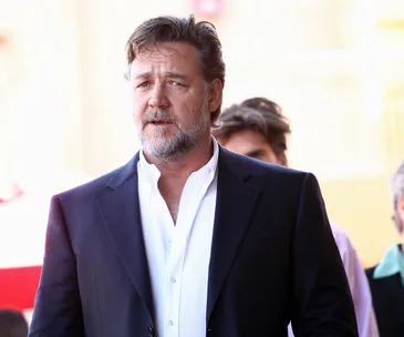 A man in a suit with a white shirt, standing outdoors, looking pensive.
