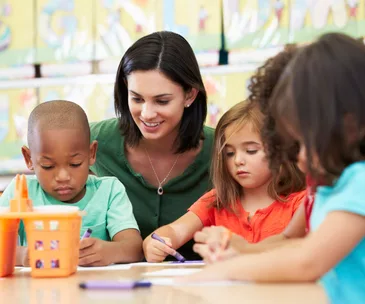 Children and teacher coloring with crayons at a classroom table.