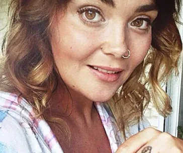 A woman with curly brown hair and a nose ring smiling gently.