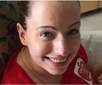 A woman smiling, wearing a red shirt, and sitting in a hospital setting.