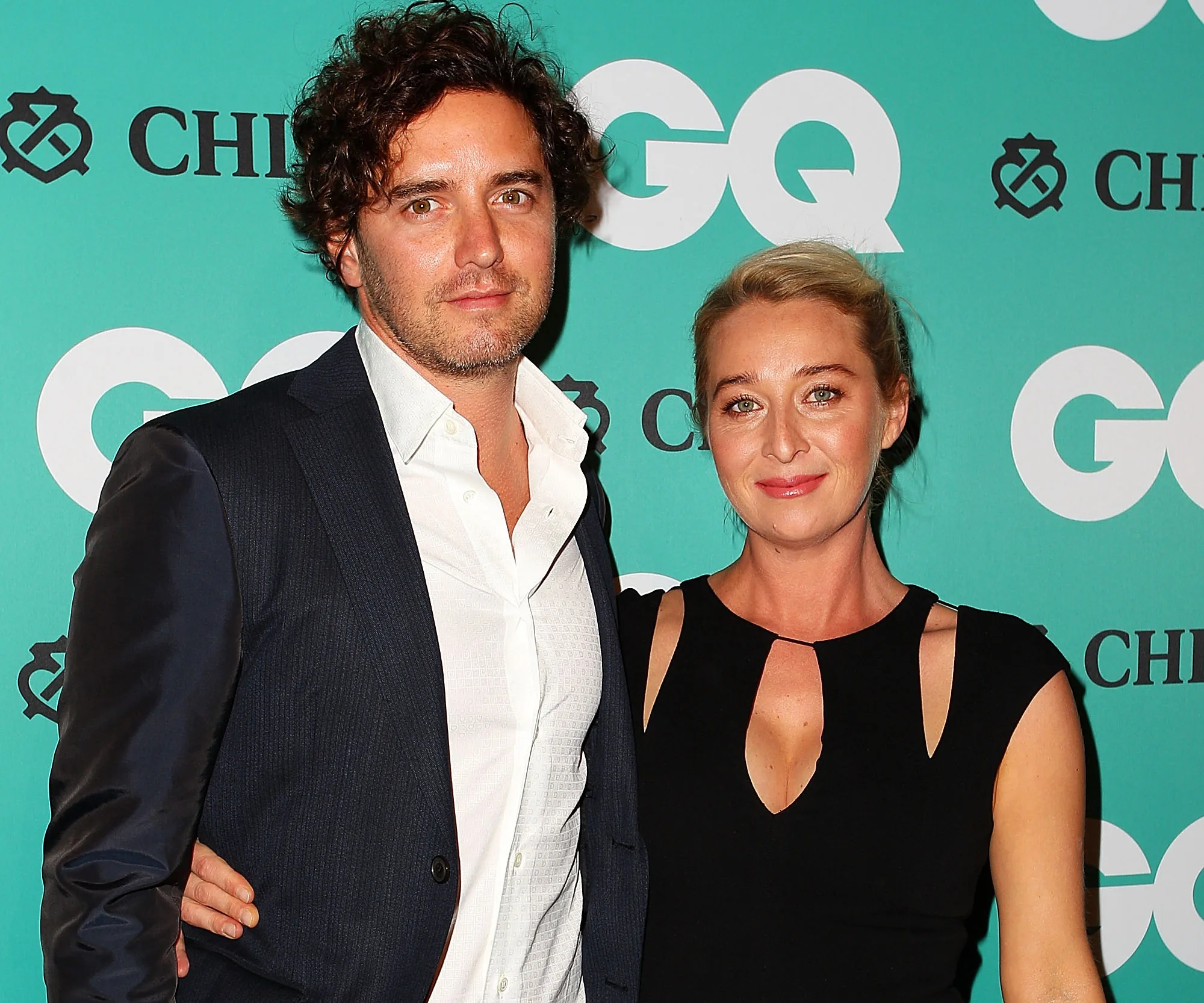 Couple posing together at a GQ event; man in suit and woman in black dress smiling at the camera.