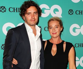 Couple posing together at a GQ event; man in suit and woman in black dress smiling at the camera.