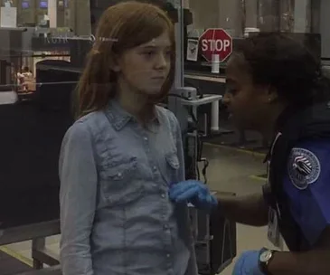 A young girl receives a security pat-down from an officer with blue gloves at an airport checkpoint.