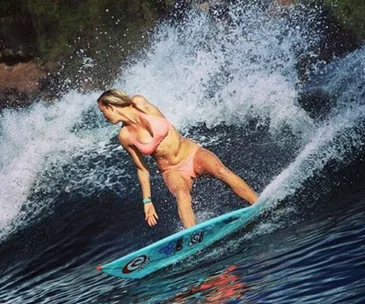 Surfer with one arm skillfully rides a large wave, showcasing strength and balance in a pink bikini.