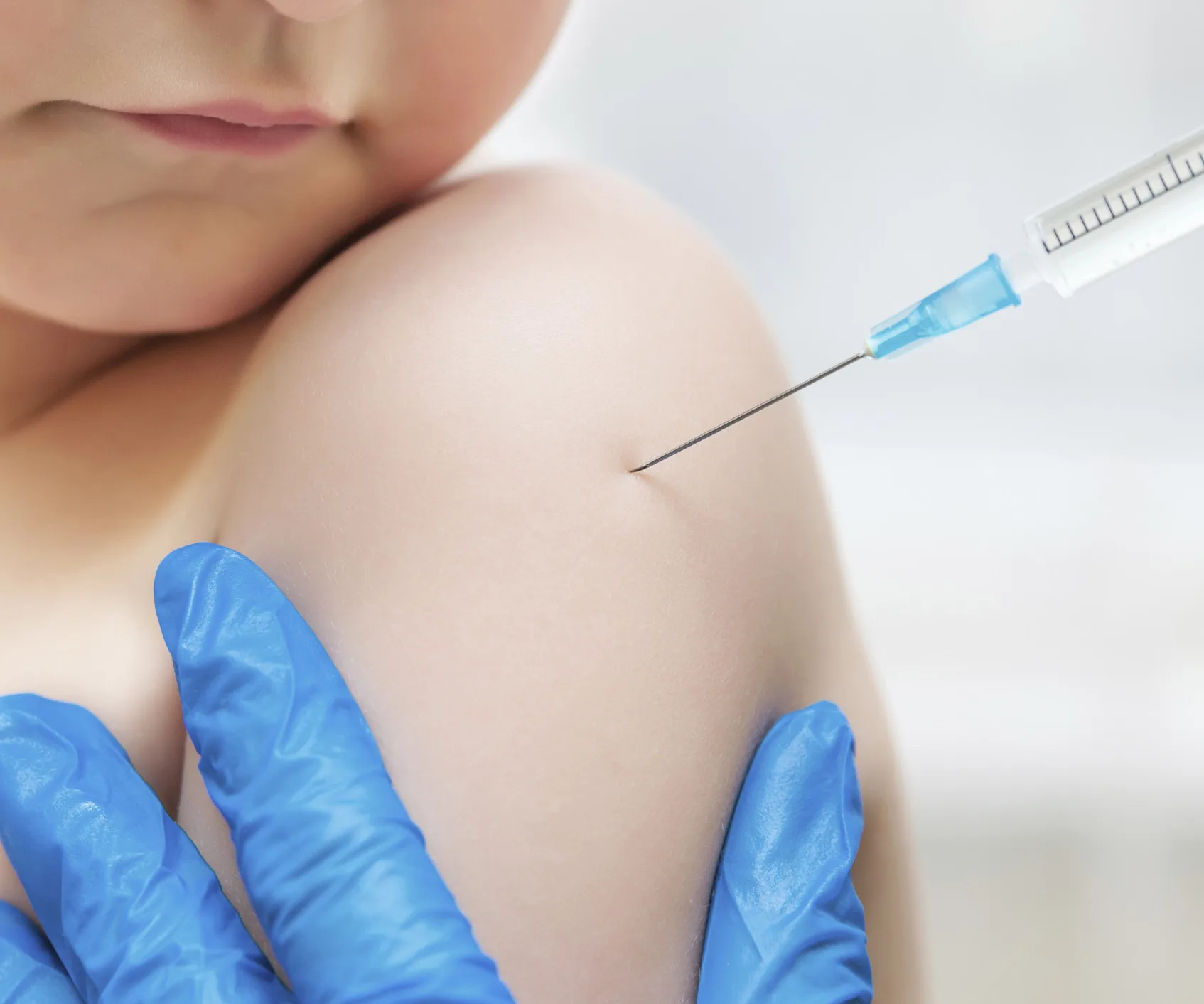 A child's arm being vaccinated with a syringe; person wearing blue gloves.