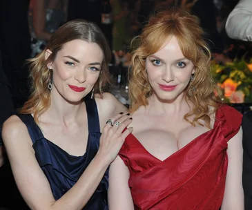 Two women posing at an event; one in a blue dress and the other in a red dress with notable details.