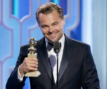 Actor in a suit holding a Golden Globe award, smiling at the podium.