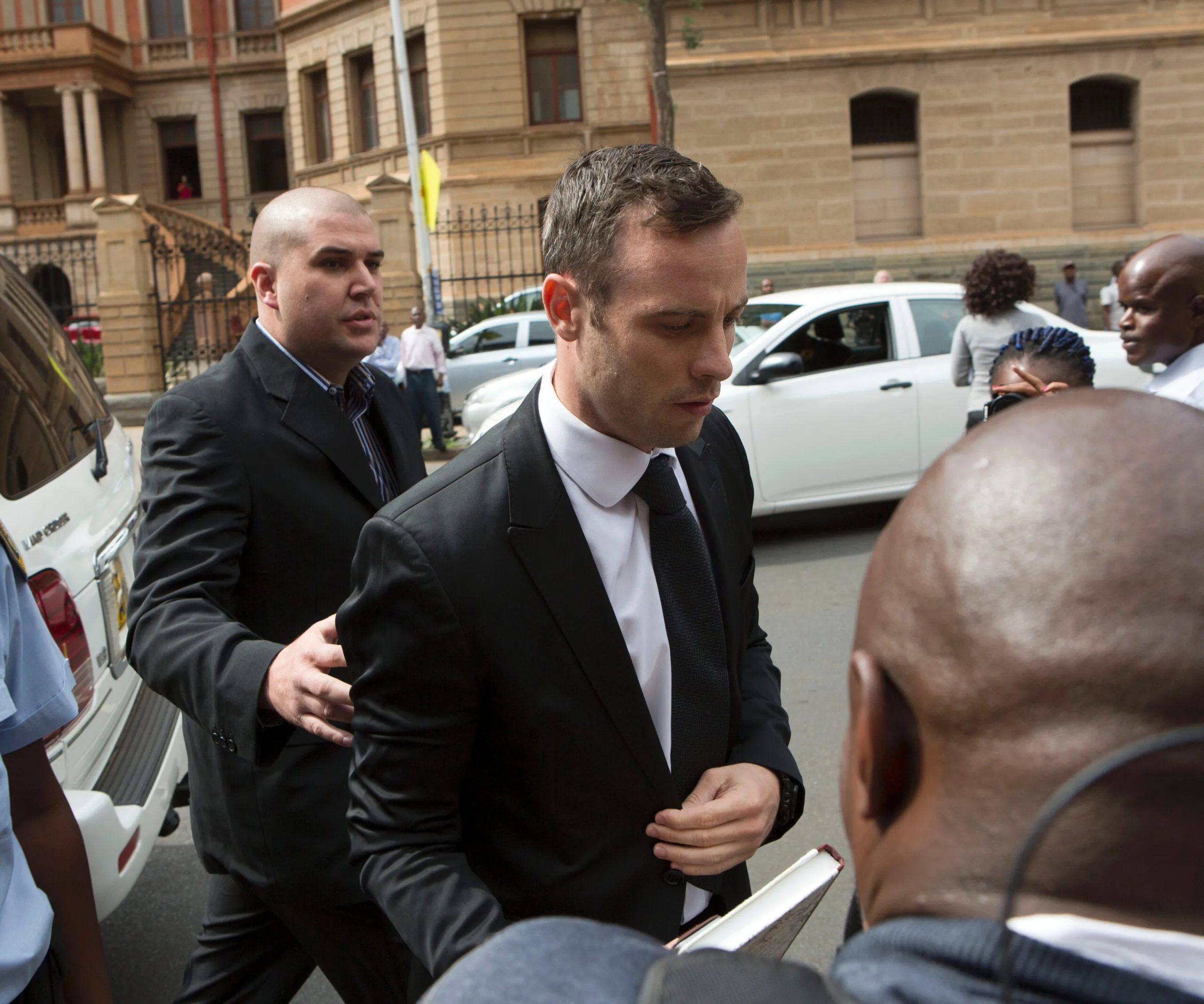 Oscar Pistorius walks outside court surrounded by people and vehicles.