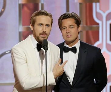 Two men in tuxedos stand at a microphone on stage during a formal award event.
