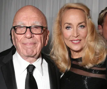 A couple smiling together at a formal event, with the man wearing glasses and a suit, and the woman in a black dress.