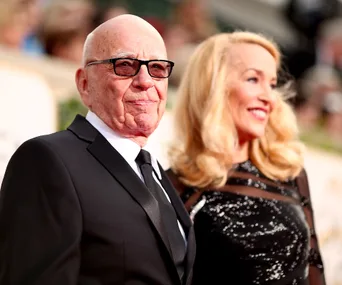 Older man in a suit and glasses with a smiling woman in a sparkly dress at an event.