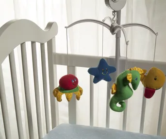 A baby crib with a colorful mobile featuring plush sea creatures and a star hanging above a blue polka dot mattress.