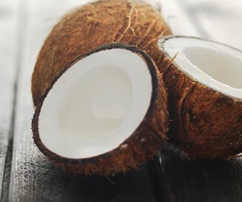 Open coconuts on a dark wooden table, showcasing white flesh inside brown shells.