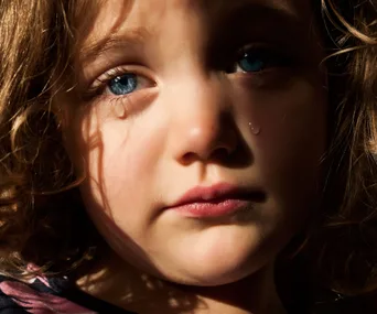 A close-up of a sad child with blue eyes and a tear on their cheek.