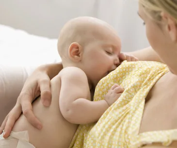 Mother breastfeeding her baby, wearing a yellow patterned top, in a close-up, intimate moment.