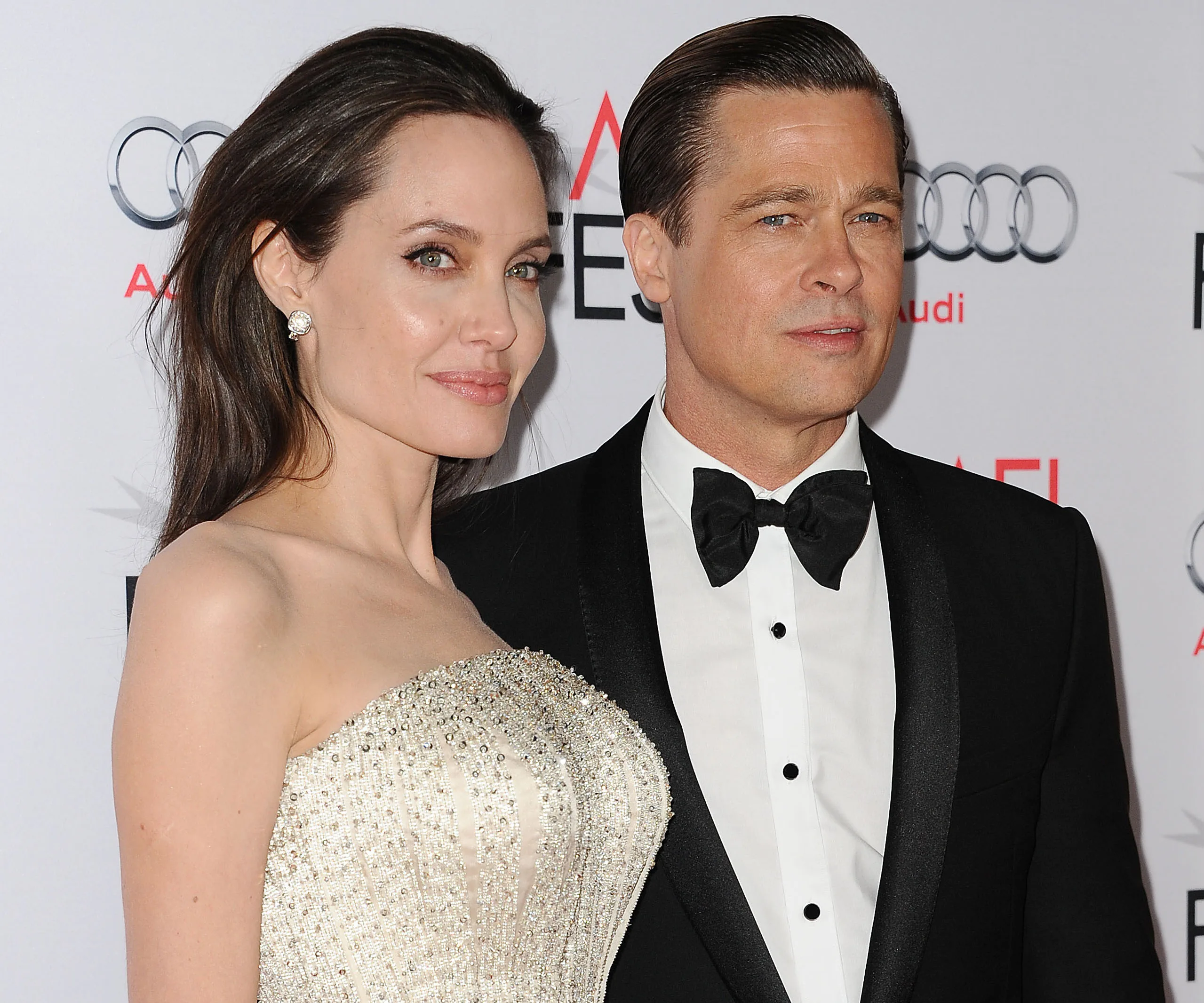 A couple dressed elegantly on the red carpet, with a backdrop featuring logos.