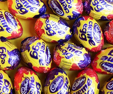 A pile of colorful Cadbury Creme Eggs in their purple, yellow, and red foil wrappers.