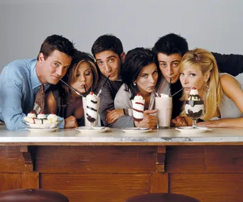 Cast of "Friends" sipping milkshakes at a diner counter, all leaning close together.