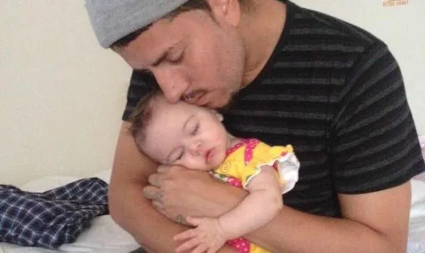 A man gently holds and kisses a sleeping baby in his arms, both appearing peaceful and content.