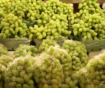 Bags and baskets of fresh green grapes displayed at a supermarket.