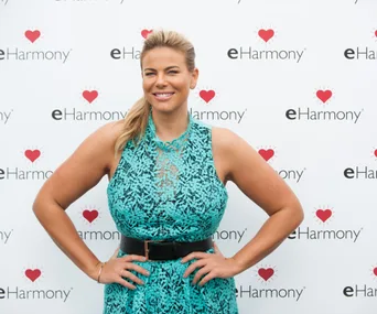 Woman in a blue lace dress smiling at an eHarmony event backdrop.