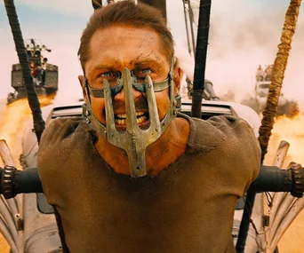 Character Max Rockatansky tied to vehicle in "Mad Max: Fury Road" action scene with fiery background.