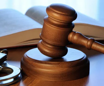 Gavel on a wooden block with handcuffs and open books in the background, symbolizing a legal setting.